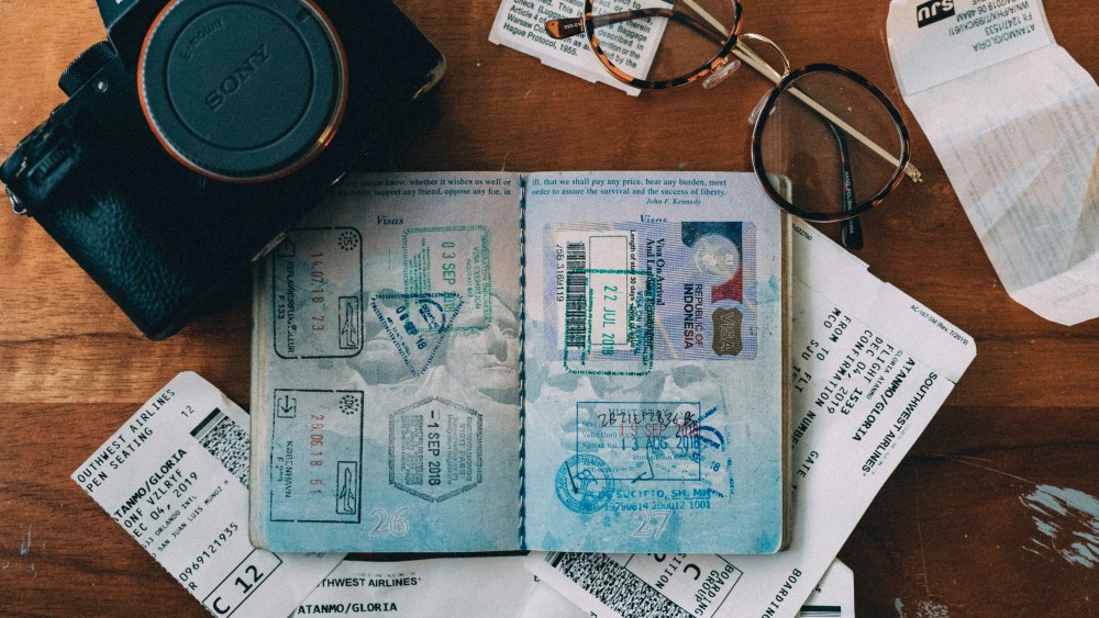 Photo of an open passport, a camera and a pair of glasses on a desk