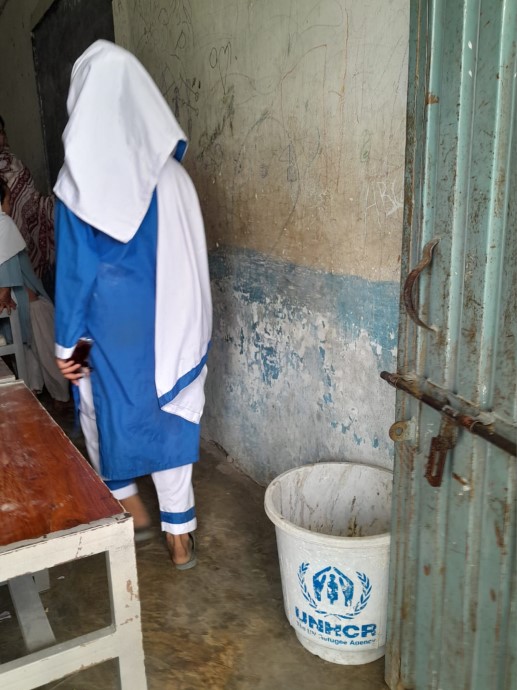 Girl dressed in white and blue. Bucket with UNHCR logo.
