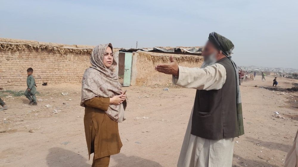Woman talking to man on a dusty road. Child playing in background.