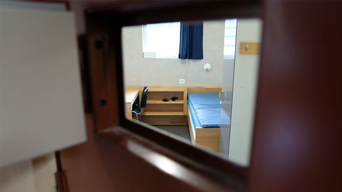 Bildet viser en fengselscelle med en seng og et bord sett fra en åpen luke i døren.