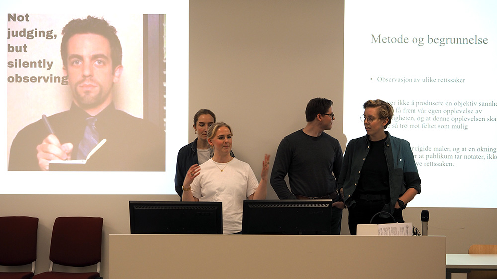 De fire studentene står sammen og presenterer det som vises på PowerPoint-presentasjonen bak dem.