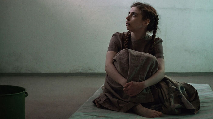Ung jente sitter på en madrass i et tomt rom av betong.