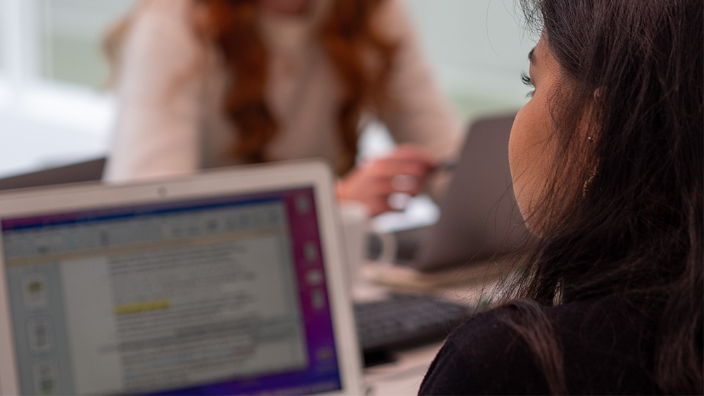 En student sitter og skriver på en oppgave som vi også ser på studentens PC-skjerm.