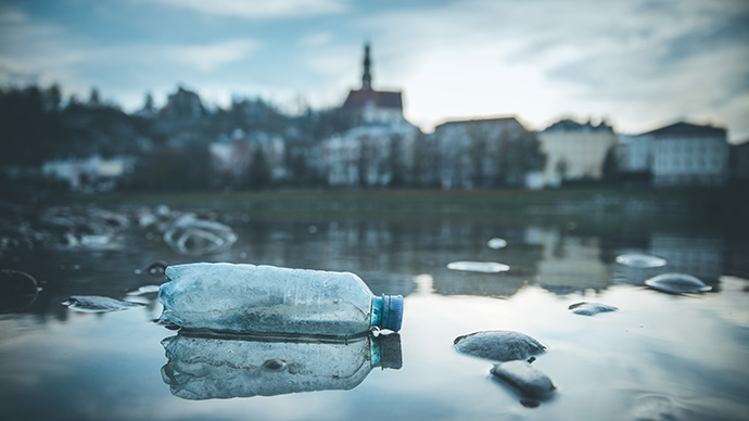 Plastflaske som flyter i en elv ved en storby.