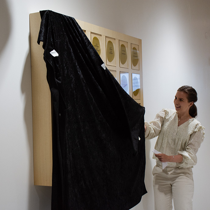 A woman is removing a black cloth from a large picture frame hanging on the wall.