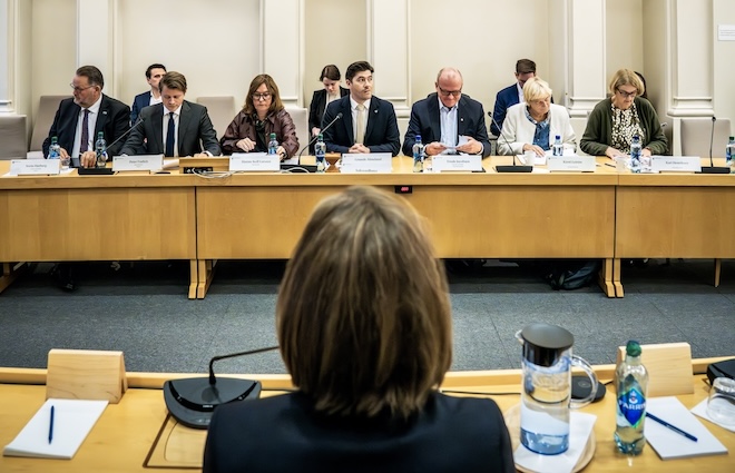 Bilde av Stortingets kontroll og konstitusjonskomité ved et bord med en person i forkant med ryggen til.