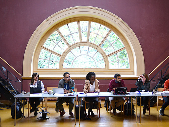 Five persons sitting behind a long table in front of a large, half-circle window. Facing the camera.